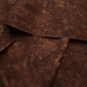 May include: Close-up of brown fabric with a marbled pattern. The fabric is folded and has a soft, textured surface.