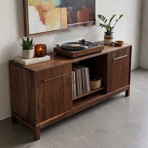 May include: A dark wood record console with a turntable, plants, and a candle on top. The console has two doors and an open shelf with records and a woven basket. A painting hangs above the console.