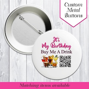 May include: A white button with the text "It's My Birthday Buy Me A Drink" in pink. The button features illustrations of various cocktails and a QR code. The words "Custom Metal Buttons" are in a pink diamond shape.