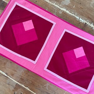 Pu&ograve; includere: Due fodere per cuscini trapuntate rosa e bordeaux con un motivo geometrico. Le fodere per cuscini hanno un bordo bianco.