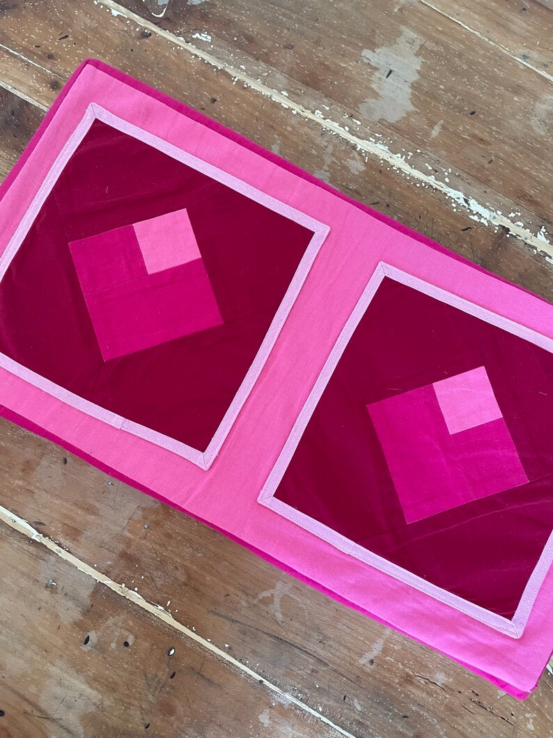 Pu&ograve; includere: Due fodere per cuscini trapuntate rosa e bordeaux con un motivo geometrico. Le fodere per cuscini hanno un bordo bianco.