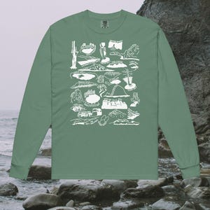 May include: A sage green long-sleeve t-shirt with a white graphic print of various landmarks and locations in Oregon. The graphic includes the names of each location.