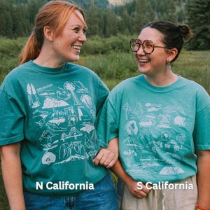 May include: Two people wearing teal blue t-shirts with white outlines of California landmarks and the text "N California" and "S California".
