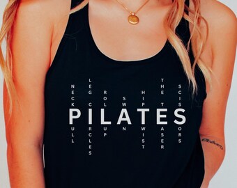 May include: Black tank top with white text that reads "PILATES" in a word search style. The text is made up of words related to pilates exercises.