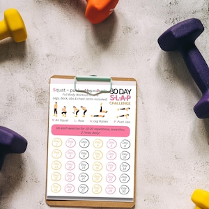 Op de afbeelding: Een fitnessafbeelding met een 30-daagse S.L.A.P. challenge workout plan op een klembord, omringd door kleurrijke dumbbells. Het workout plan bevat oefeningen zoals air squats, roeien, beenheffen en push-ups. De dumbbells zijn geel, oranje en paars.
