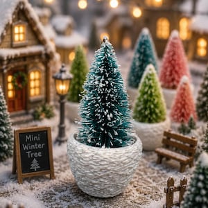 Könnte beinhalten: Ein künstlicher Miniatur-Tannenbaum mit grünen Nadeln, die mit weißem Schnee bestäubt sind, in einem strukturierten weißen Topf. Daneben steht ein kleines Holzschild mit dem Text Mini Winter Tree und einem Baum-Symbol in einer verschneiten Dorflandschaft.