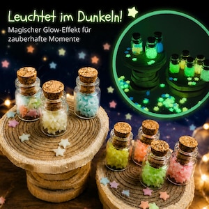 May include: Small glass jars with cork stoppers filled with tiny star-shaped pieces in various pastel colors. The text Leuchtet im Dunkeln and Magischer Glow-Effekt f&uuml;r zauberhafte Momente appears at the top. The jars are displayed on wooden slices.