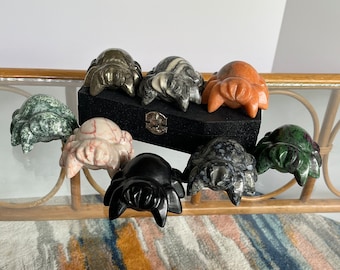 May include: A set of eight hand-carved stone spider figurines. The spiders are made of various types of stone, including green, black, white, and red. The spiders are all different sizes and shapes, and they are arranged in a circle on a wooden table.