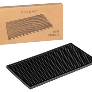 Könnte beinhalten: Schwarze Barista-Tampermatte mit strukturierter Oberfläche. Die Matte besteht aus Gummi und hat ein erhabenes Muster aus kleinen Kreisen. Die Matte ist so konzipiert, dass sie Arbeitsplatten vor Kratzern und Verschüttungen schützt. Die Verpackung zeigt den Markennamen "NATUMO" und den Text "Barista Tamper Mat".