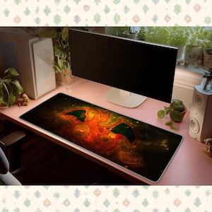 Peut inclure: Un tapis de bureau rectangulaire orné d'un motif orange et noir représentant une créature ailée semblable à un dragon, sur un fond de nébuleuse sombre et étoilée. Le tapis est posé sur un bureau rose devant un écran d'ordinateur.