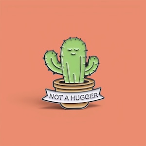 May include: A green cactus pin in a brown pot with the text "NOT A HUGGER" on a white banner. The cactus has a smiling face and black outlines. The background is a solid orange color.