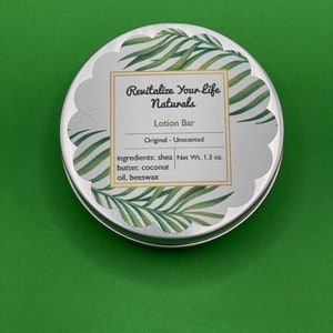 May include: A silver tin with a white label that reads "Revitalize Your Life Naturals Lotion Bar Original - Unscented Ingredients: shea butter, coconut oil, beeswax Net Wt. 1.3 oz."