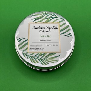 May include: A silver tin with a white label that reads "Revitalize Your Life Naturals Lotion Bar Lavender Vanilla Net Wt. 1.3 oz." The label has a green tropical leaf design.