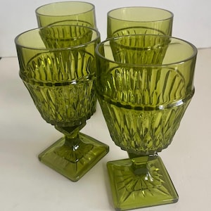 May include: Set of four green-tinted glass goblets. Each goblet features a diamond-patterned bowl, a square base, and a short stem. The glasses have a vintage aesthetic and are suitable for serving beverages.