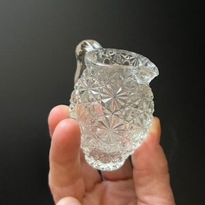 Könnte beinhalten: Ein kleiner, durchsichtiger Glaskännchen mit einem Diamantenmuster. Der Kännchen hat einen Griff und einen abgerundeten Körper.