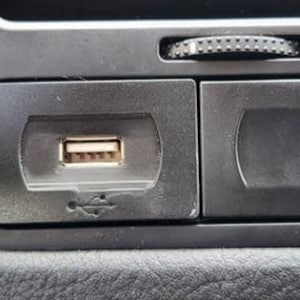 Könnte beinhalten: Nahaufnahme einer schwarzen Autokonsole mit einem USB-Anschluss und einem kleinen Staufach. Der USB-Anschluss ist rechteckig mit einem sichtbaren Stecker. Ein kleines Rad befindet sich über den Fächern.