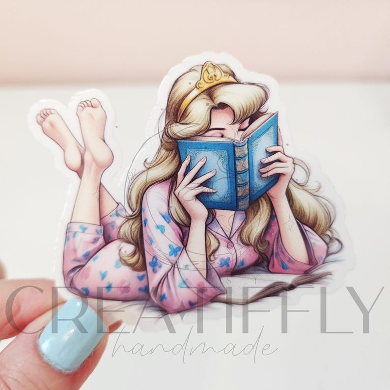 May include: A sticker featuring a cartoon illustration of a woman with long blonde hair wearing a gold crown and pink pajamas with blue butterfly patterns. She is lying down and reading a blue book.
