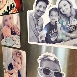 May include: A collection of family photos on a silver refrigerator. The photos are in black and white and color. The photos show a family of four, including a father, mother, and two sons. The photos are arranged in a grid pattern.