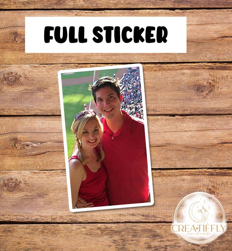May include: A couple in red shirts smiles for a photo at a baseball game. The photo is printed on a sticker.