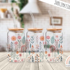 May include: Three clear glass tumblers with bamboo lids and matching straws. Each tumbler features a floral pattern with pink, orange, and green flowers and leaves. The tumblers are arranged in a row on a wooden surface. The text "SUBLIMATION PRINT" is visible at the top of the image.