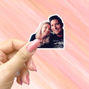 May include: A sticker featuring a photo of a couple smiling at the camera. The woman is wearing a black shirt and the man is wearing a black shirt with the text "The Lady P. & Sons" printed on it.