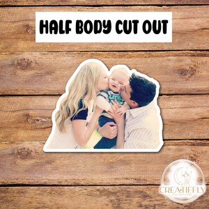 May include: A photo cutout of a family with a woman, a man, and a baby. The woman is kissing the baby on the cheek. The man is holding the baby and smiling. The baby is wearing a blue and green shirt. The family is standing in front of a green background.