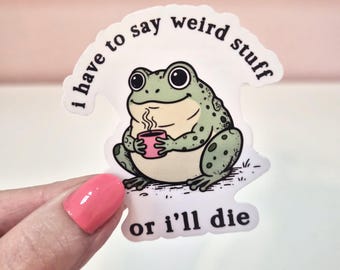 Pode incluir: Um adesivo de vinil cortado com o formato de um sapo verde-claro com manchas escuras segurando uma pequena caneca rosa com vapor saindo. O texto "i have to say weird stuff or i'll die" está impresso em preto ao redor do sapo.