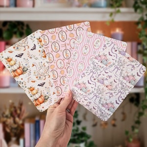 May include: Three rectangular sheets of paper featuring decorative patterns with geese, pumpkins, bats, and floral elements in shades of orange, pink, and purple. The designs include oval frames, vertical stripes, and repeating motifs on a light background.