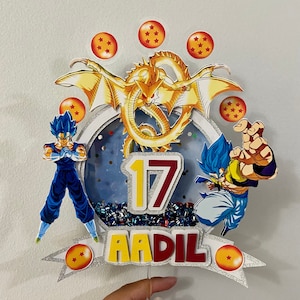 Peut inclure: Un cake topper coloré avec des personnages de Dragon Ball Z et un dragon doré. Le design comprend le chiffre 17 et le nom "AADIL" en lettres grasses, entouré de paillettes et de boules en forme d'étoiles.