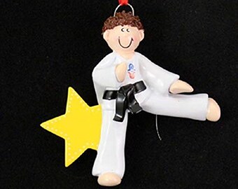 May include: A white and black karate ornament with a yellow star. The figure is wearing a white uniform with a black belt and is kicking with their right leg.