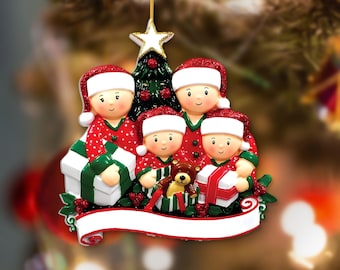 May include: A Christmas tree ornament featuring a family of four wearing red and white Santa hats and matching pajamas. The figures are positioned in front of a green Christmas tree with a gold star topper, holding wrapped gifts and a teddy bear.