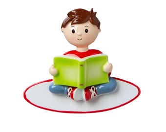 Op de afbeelding: Een jongensfiguur dat op een wit ovaal tapijt met een rode rand zit en een groen boek vasthoudt. Hij draagt een rood shirt, een blauwe spijkerbroek en rode schoenen.