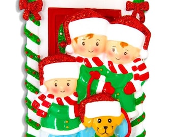 May include: A Christmas ornament featuring a family of three standing in front of a red door with a dog. The family is wearing green coats, red hats, and white scarves. The dog is wearing a red hat and a white scarf. The ornament is decorated with glitter and has a white background.