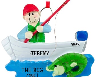May include: A personalized Christmas ornament featuring a cartoon fisherman in a boat with a fishing rod and a large fish. The ornament is blue, green, white, and red. The text on the ornament reads "Jeremy, The Big One!" and "YEAR".