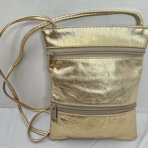 Puede incluir: Un bolso bandolera dorado con un acabado texturizado. El bolso tiene dos compartimentos con cremallera y una correa fina y ajustable. Hay un asa pequeña en la parte superior. El bolso está hecho de un material brillante y metálico.