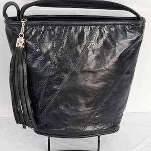 Può includere: Una borsa a secchiello in pelle nera con un lungo pendente. La borsa ha un design trapuntato e un manico superiore.