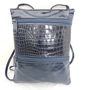 Puede incluir: Un bolso bandolera azul marino con acabado brillante. El bolso presenta un patrón texturizado similar al de un cocodrilo en la sección central y dos compartimentos con cremallera. Tiene correas finas.