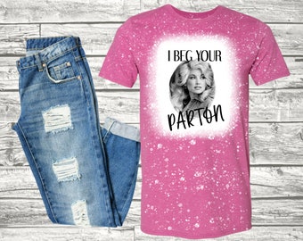 May include: A pink t-shirt with a white bleach design featuring a black and white image of Dolly Parton with the text "I beg your Parton".