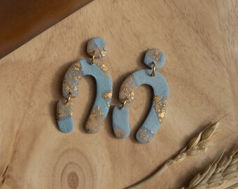 May include: A pair of blue and gold statement earrings with a unique arch shape. The earrings are made of polymer clay and have a textured finish.