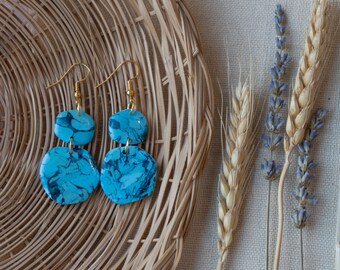 May include: A pair of blue and white marbled earrings with gold hooks. The earrings are made of two round pieces of marbled clay.