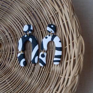 May include: A pair of black and white statement earrings with a geometric design. The earrings are made of polymer clay and have a unique, abstract shape.