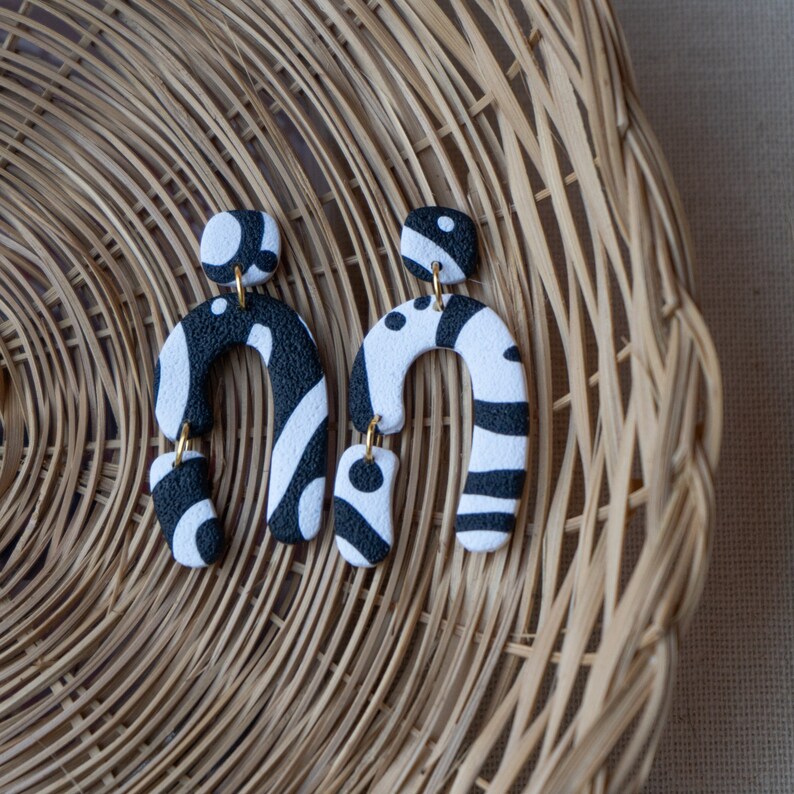 May include: A pair of black and white statement earrings with a geometric design. The earrings are made of polymer clay and have a unique, abstract shape.