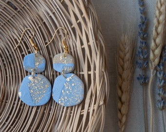 May include: A pair of blue and gold earrings with a textured finish. The earrings are made of two pieces, one larger than the other, and are connected by a gold loop. The earrings are hanging from a gold hook.