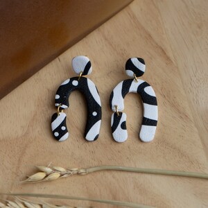 May include: A pair of black and white patterned dangle earrings. The earrings are made of polymer clay and have a unique abstract design.