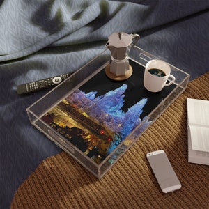 May include: A clear acrylic tray with a black background and a colorful image of a city skyline at night. The tray also includes a silver coffee pot, a white mug with coffee, and a black remote control.