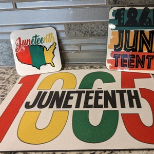 May include: A set of three Juneteenth themed coasters. The coasters are made of a white material with red, yellow, and green accents. The largest coaster features the text "Juneteenth" in black lettering. The other two coasters feature the text "Juneteenth" and "1865" in black lettering.