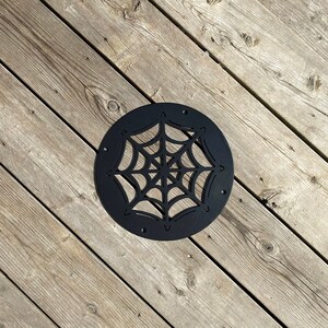 May include: Black metal round decorative wall decor with a cutout spider web design.
