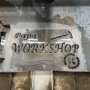 May include: A metal sign with the words "Papa's Workshop" cut out. The sign also features a hammer and a wrench and gear design.