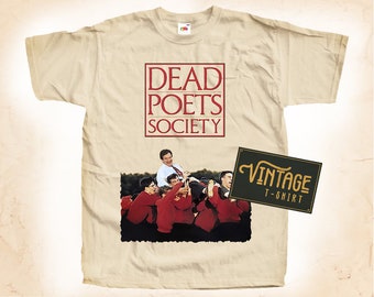 May include: Cream-colored t-shirt featuring the text "DEAD POETS SOCIETY" in a red square. Below the text is a picture of a group of people. A vintage t-shirt label is on the right.