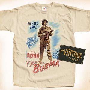May include: Cream-colored t-shirt featuring a vintage movie poster design. The poster depicts a soldier holding a gun, with the text "Objective Burma" and "Warner Bros." printed on the shirt. A "Vintage T-Shirt" label is also present.